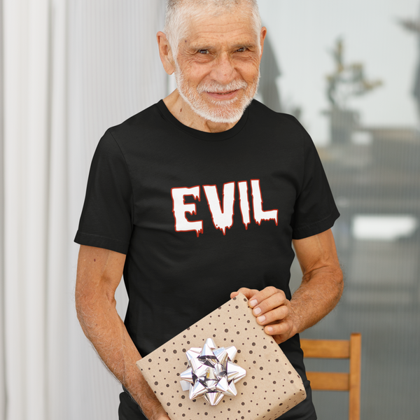 An older man with a white beard stands behind a dining table holding a wrapped gift box. He is wearing a black t-shirt with the word 'EVIL' printed in a dripping red-and-white font.