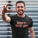Man wearing a black t-shirt with 'DON'T GIVE UP!' text, standing against a metal wall.