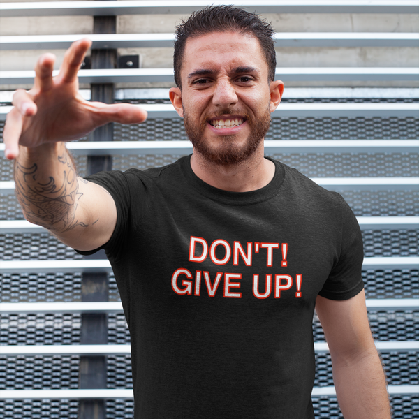 Man wearing a black t-shirt with 'DON'T GIVE UP!' text, standing against a metal wall.